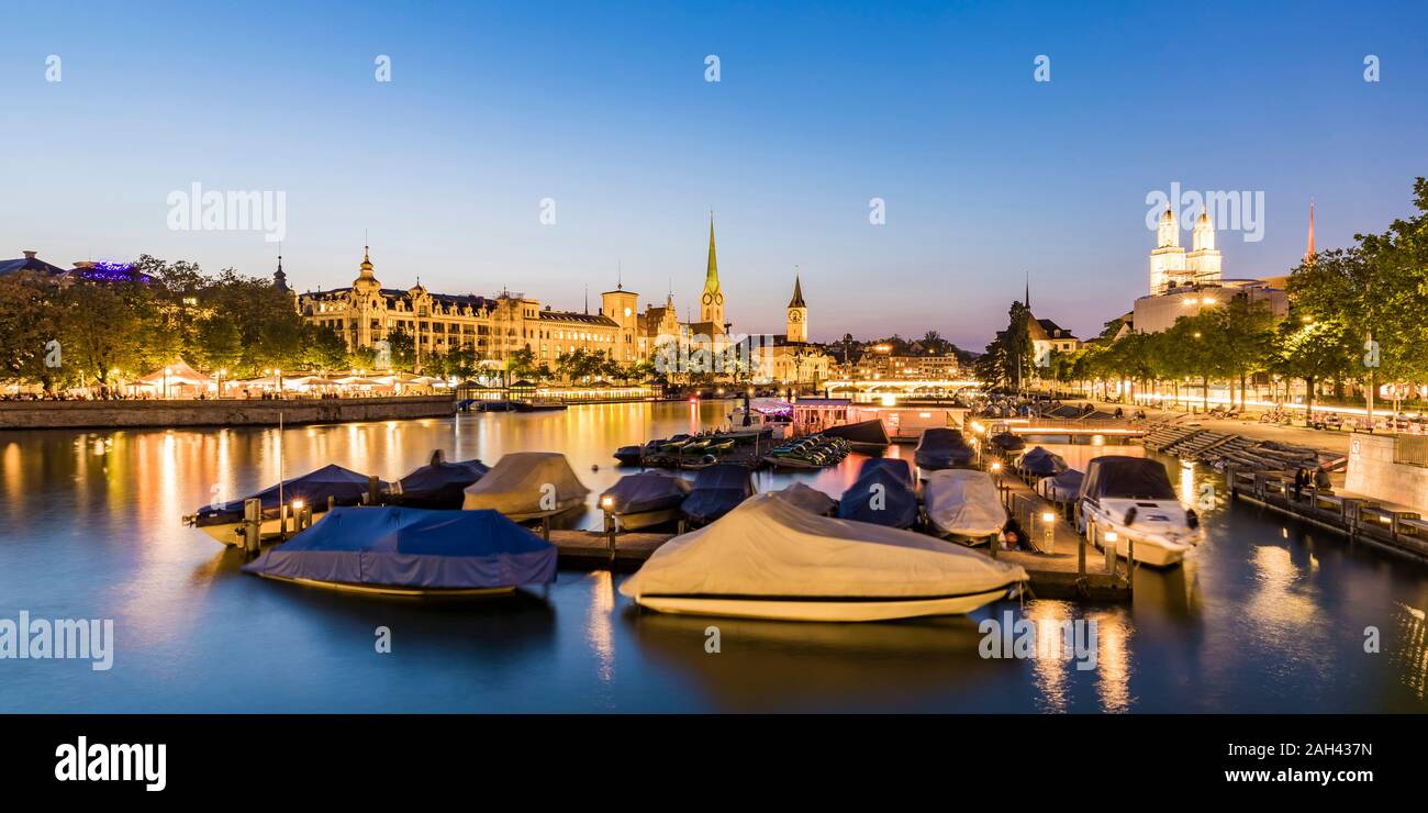 Suiza, en el cantón de Zurich, Zurich, cubiertas embarcaciones amarradas en el río Limmat al anochecer con el Old Town Waterfront en segundo plano. Foto de stock