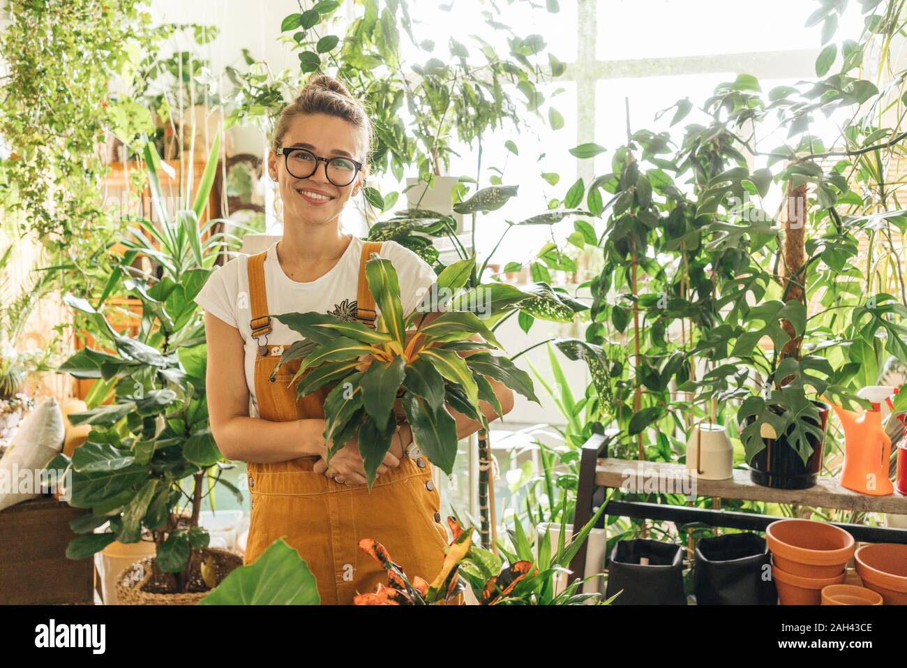 Retrato de una mujer sonriente sosteniendo una planta en una pequeña tienda de jardinería Foto de stock