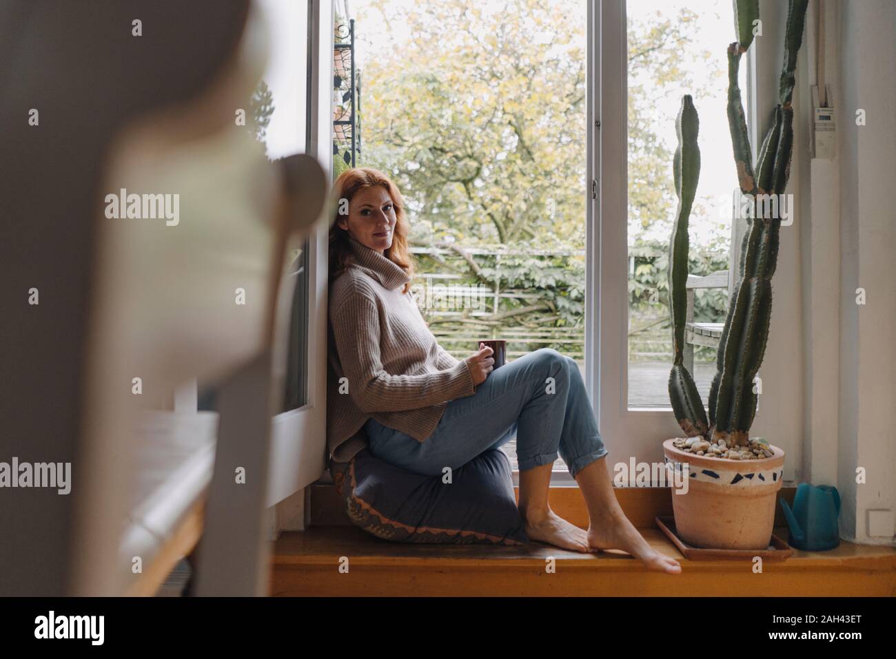 Mujer madura sentada sobre los pasos de la puerta del balcón, bebiendo café Foto de stock