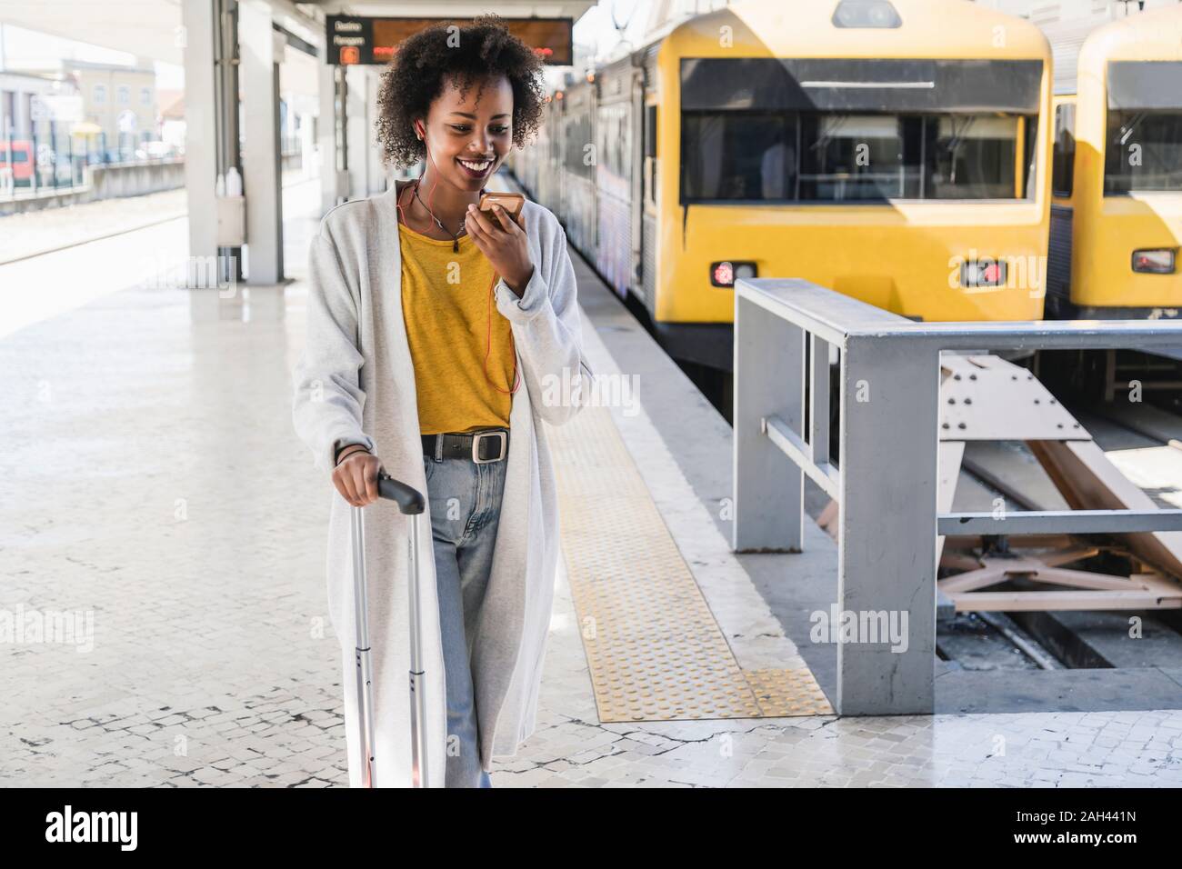 Mujer sonriente con auriculares mediante smartphone en la plataforma de la estación Foto de stock