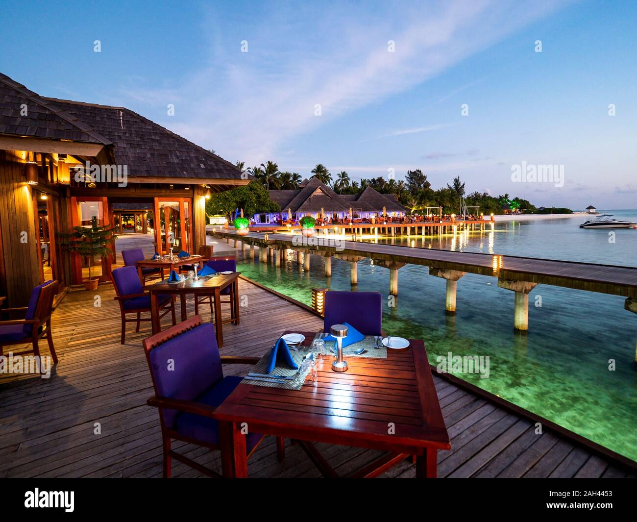 Maldivas, mesas de comedor del restaurante costero al anochecer con el muelle en segundo plano. Foto de stock