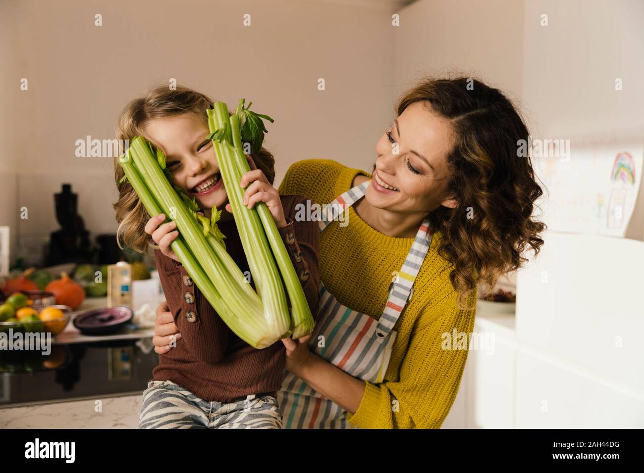 Juguetón niña con su madre sosteniendo el apio en la cocina Foto de stock