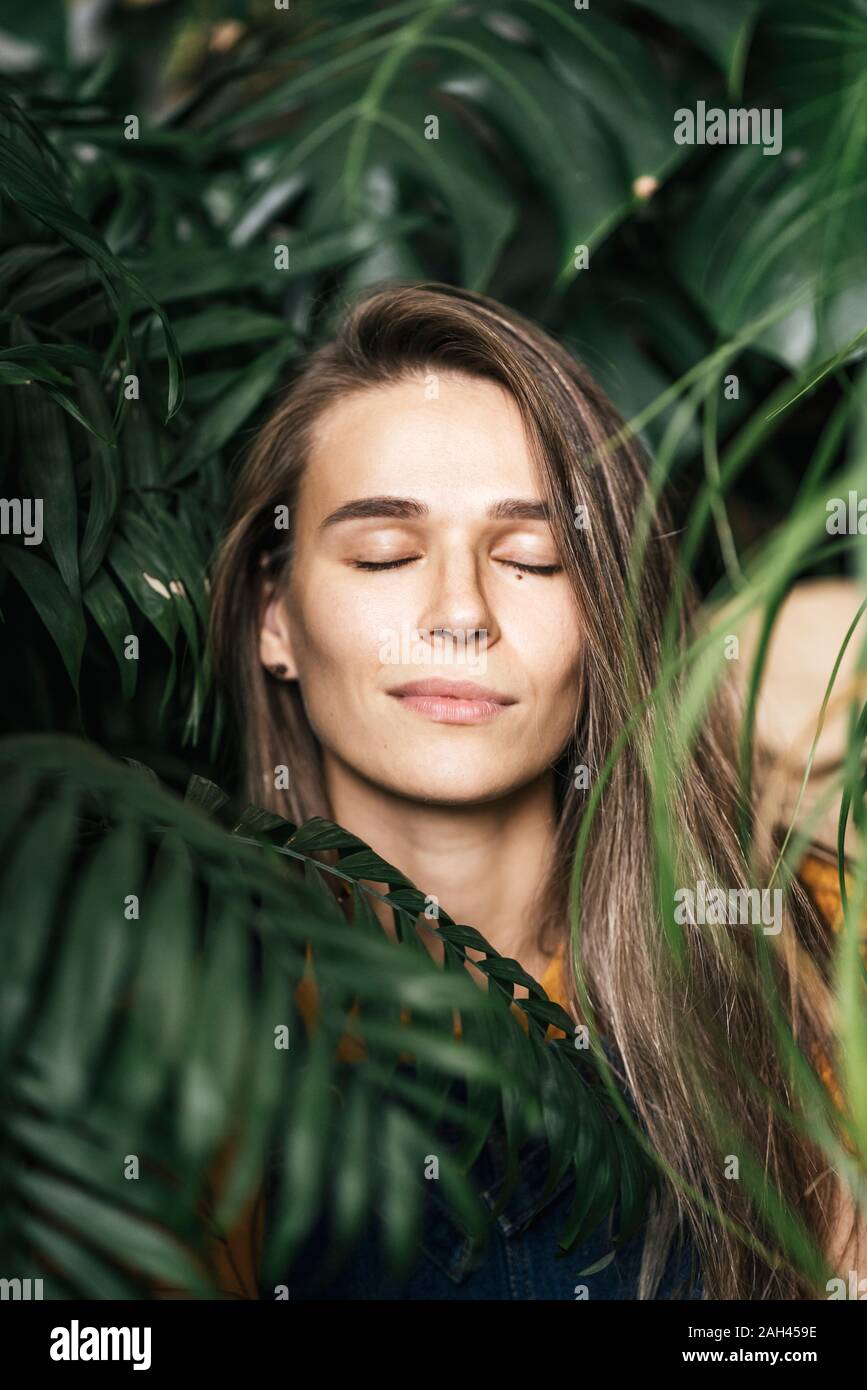 Retrato de una mujer joven con los ojos cerrados en medio de plantas verdes. Foto de stock