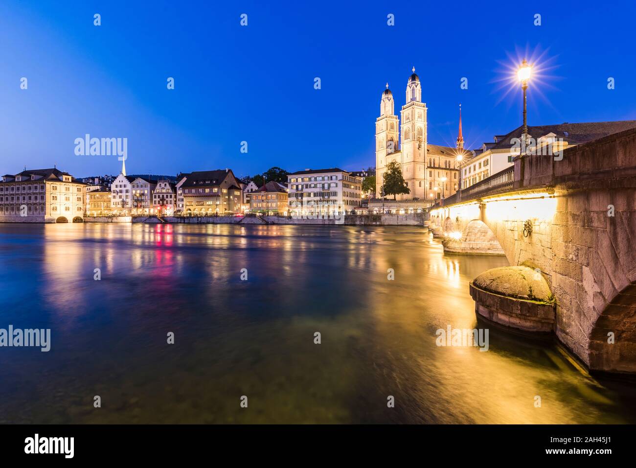 Suiza, en el cantón de Zurich, Zurich, el Río Limmat, Munsterbrucke y casco antiguo edificios junto a la calle Limmatquai iluminada al atardecer Foto de stock