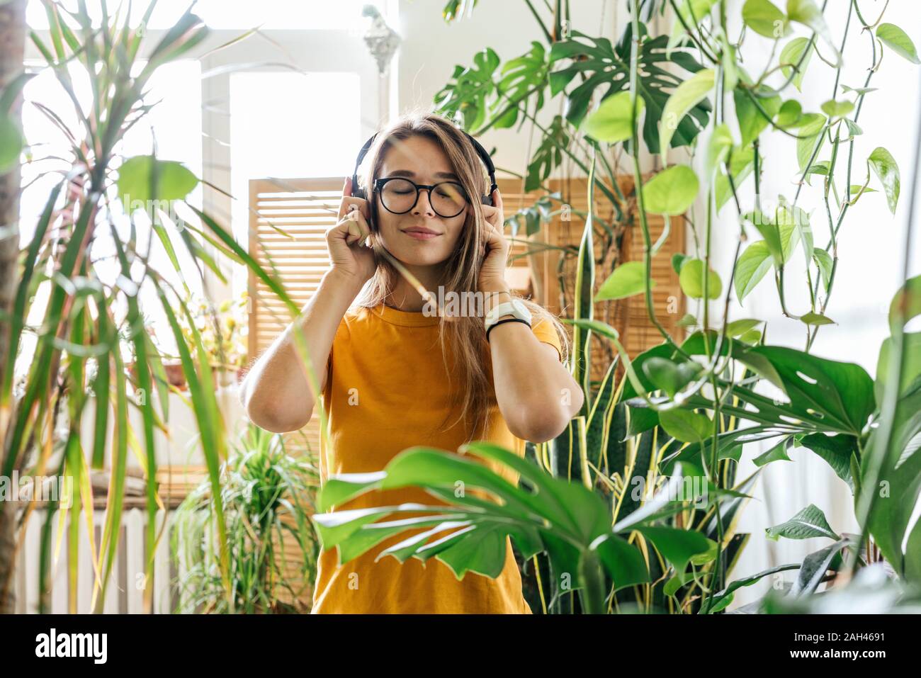 Mujer joven rodeada por plantas escuchar música con auriculares Foto de stock