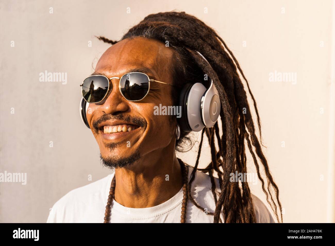 Retrato del hombre maduro sonriente con dreadlocks y auriculares, escuchando música y mirando hacia los lados Foto de stock