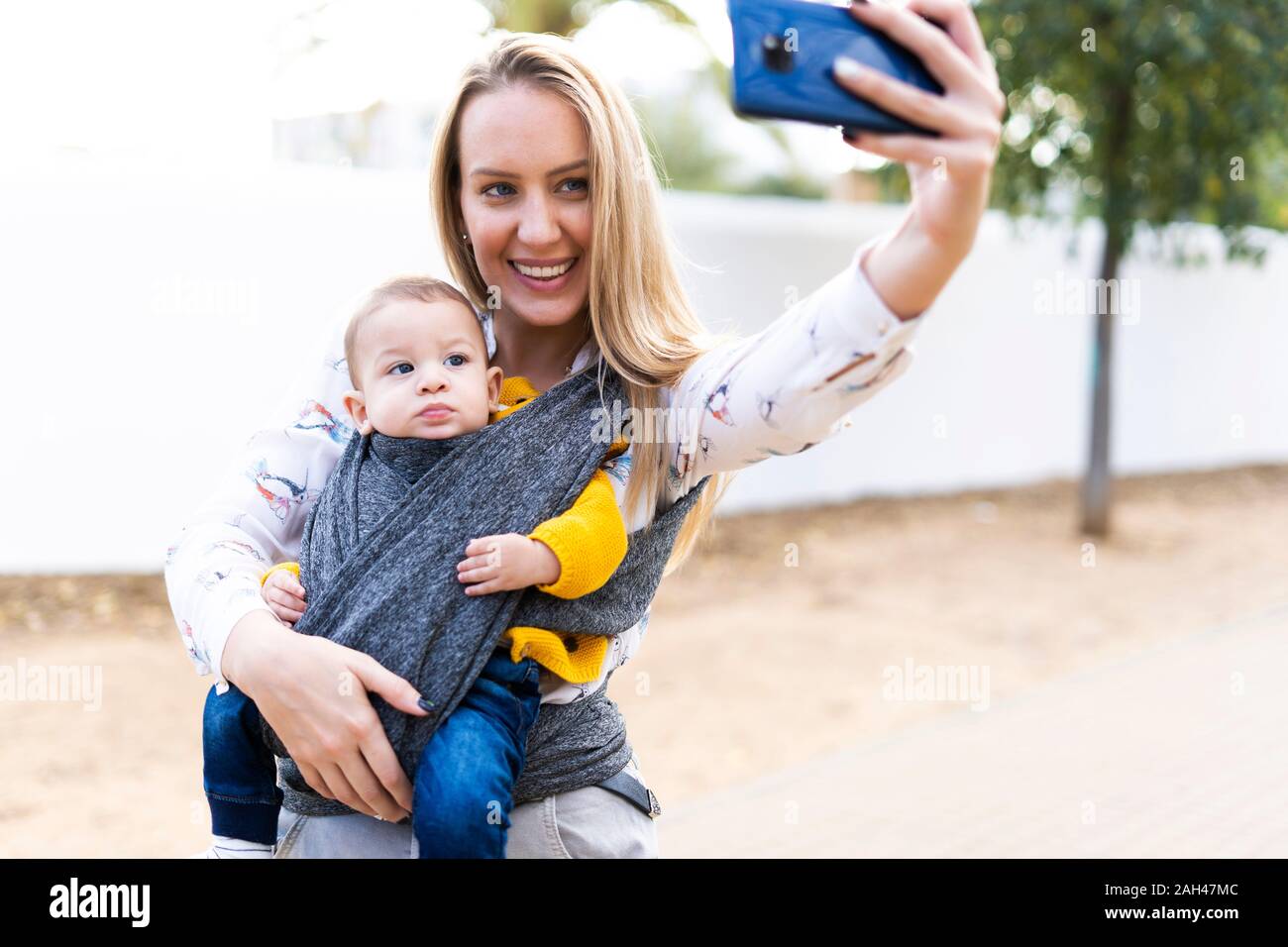 Feliz madre con Baby Boy en un cabestrillo tomando un selfie Foto de stock