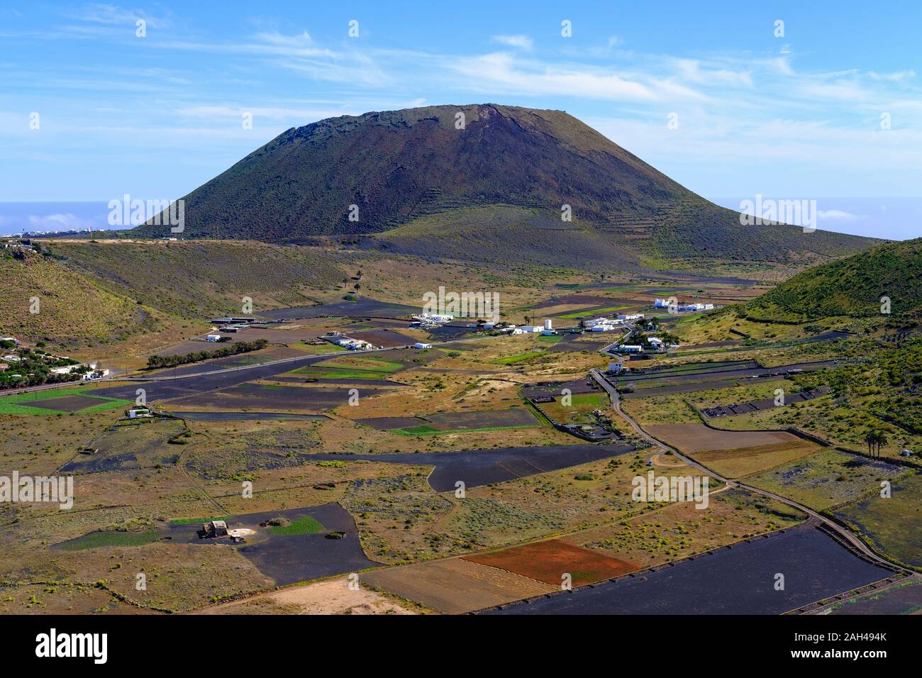 España, Islas Canarias, Guinate, campos delante de aldea rural con volcán Monte Corona asomándose en segundo plano. Foto de stock