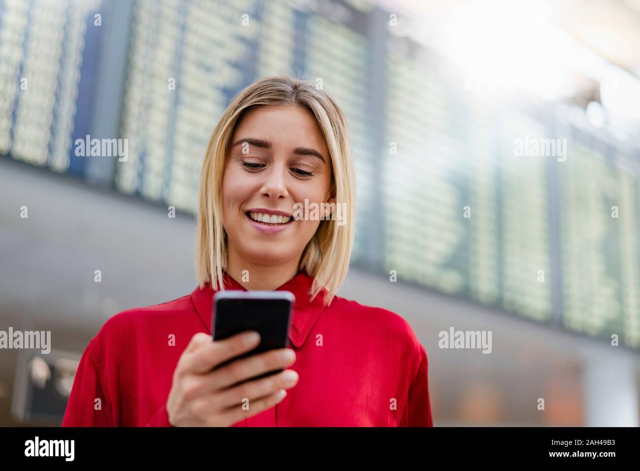 Sonriente joven empresaria mediante celular en llegada salida junta en el aeropuerto Foto de stock