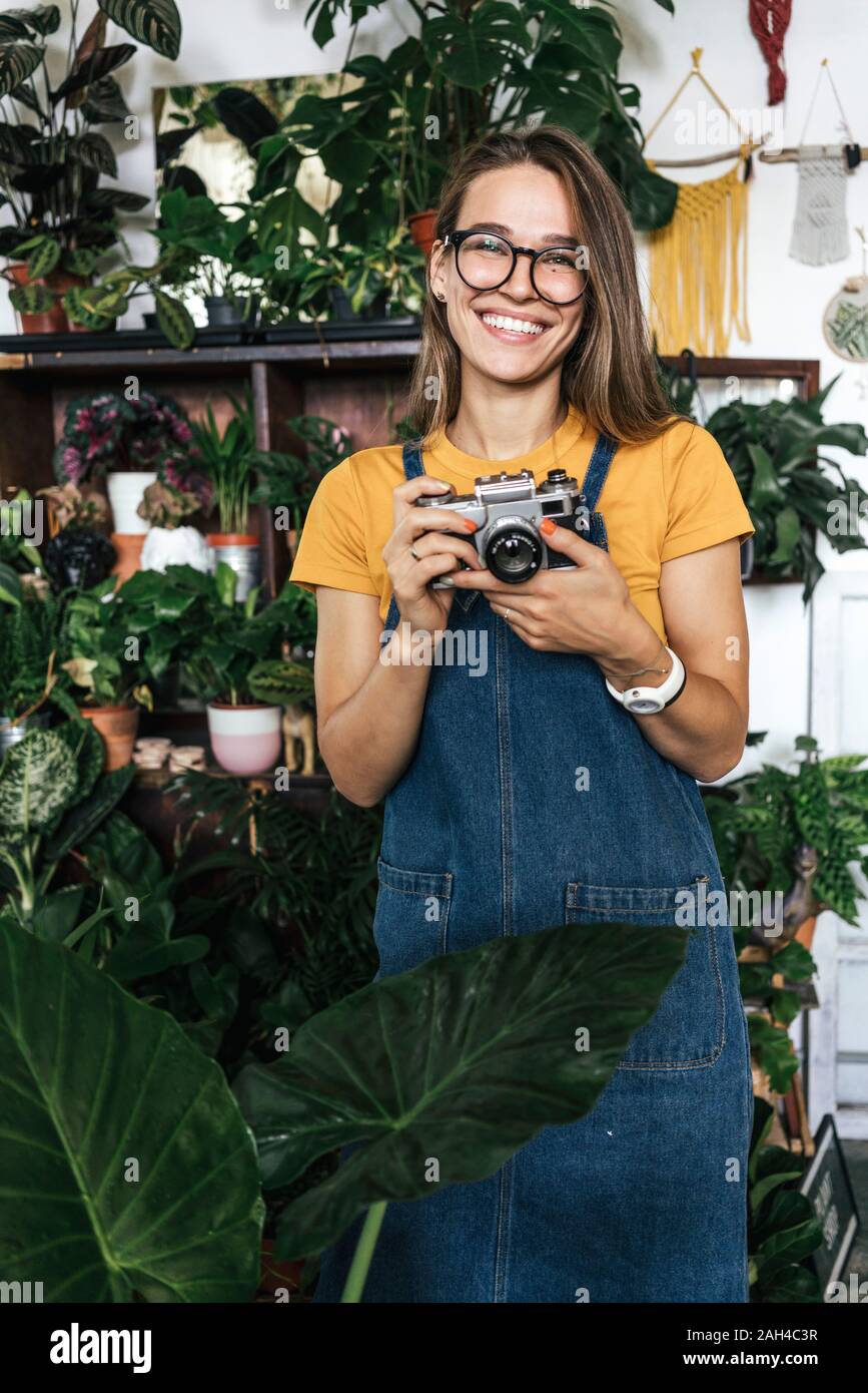 Retrato de una joven feliz con una cámara en una pequeña tienda de jardinería Foto de stock