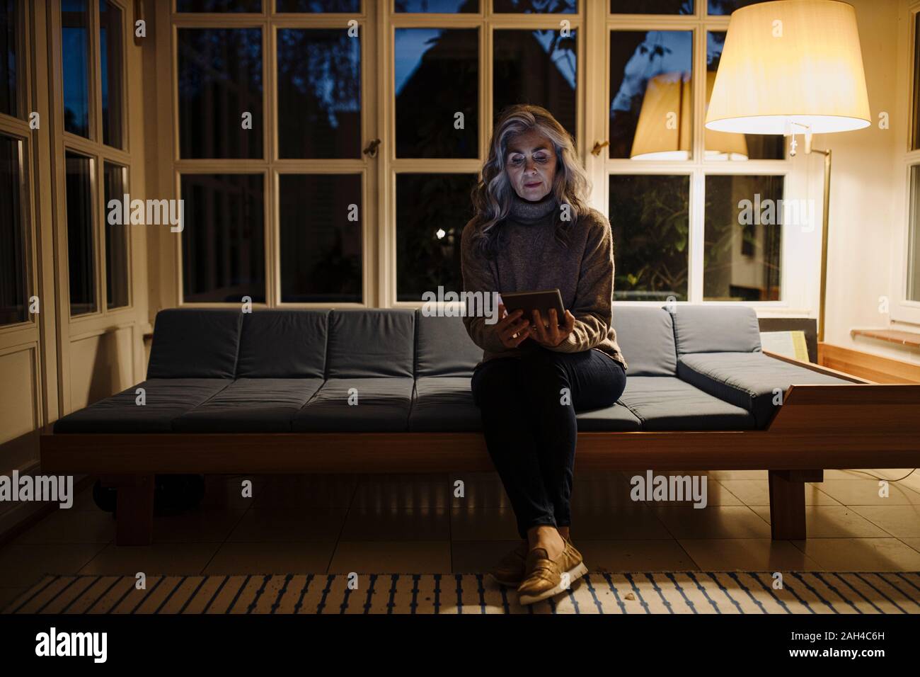 Mujer madura con tablet de sofá en casa en la oscuridad Foto de stock