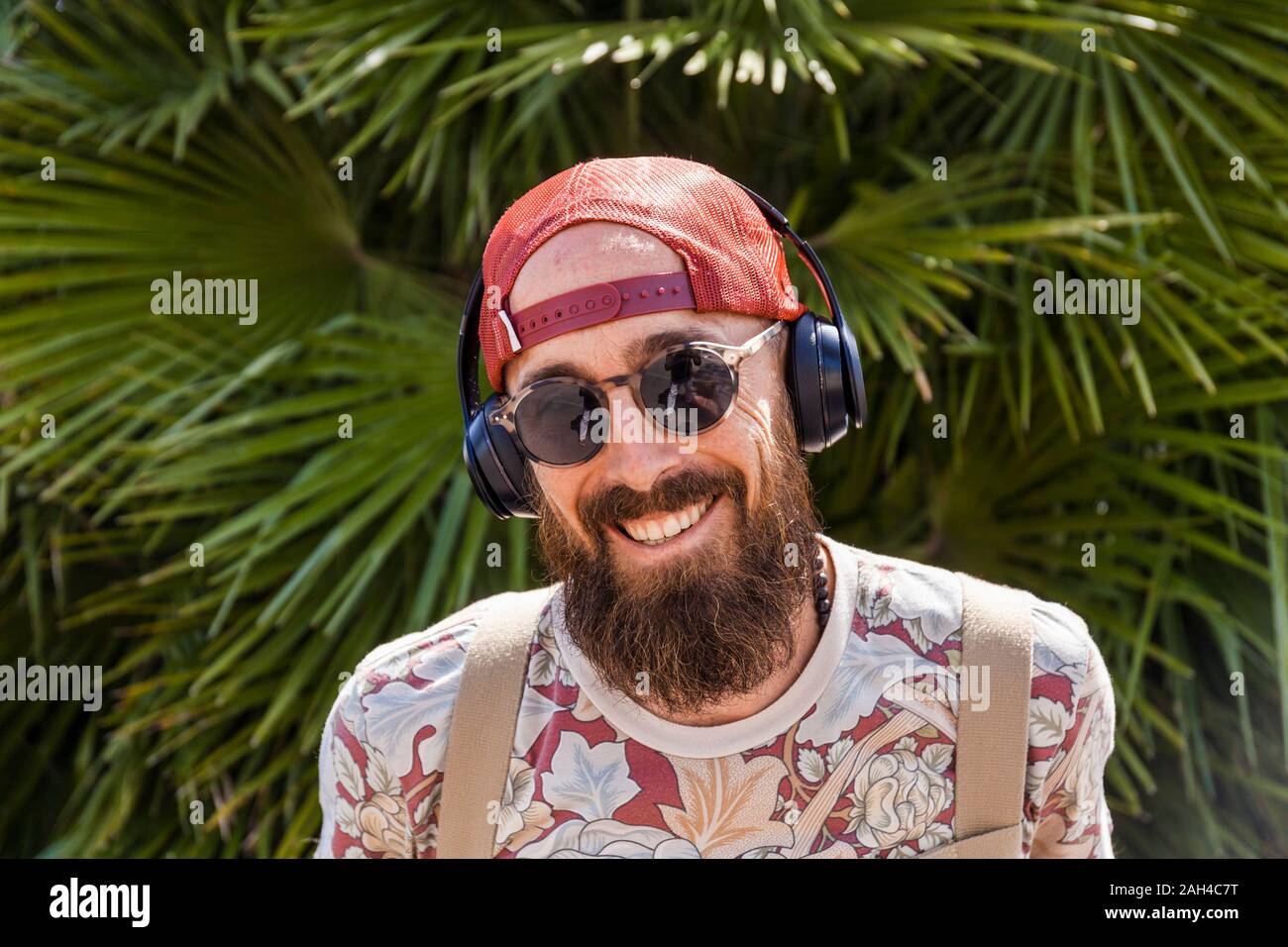 Sonriente hombre maduro con rojo basecap, gafas de sol y Auriculares blancos Foto de stock