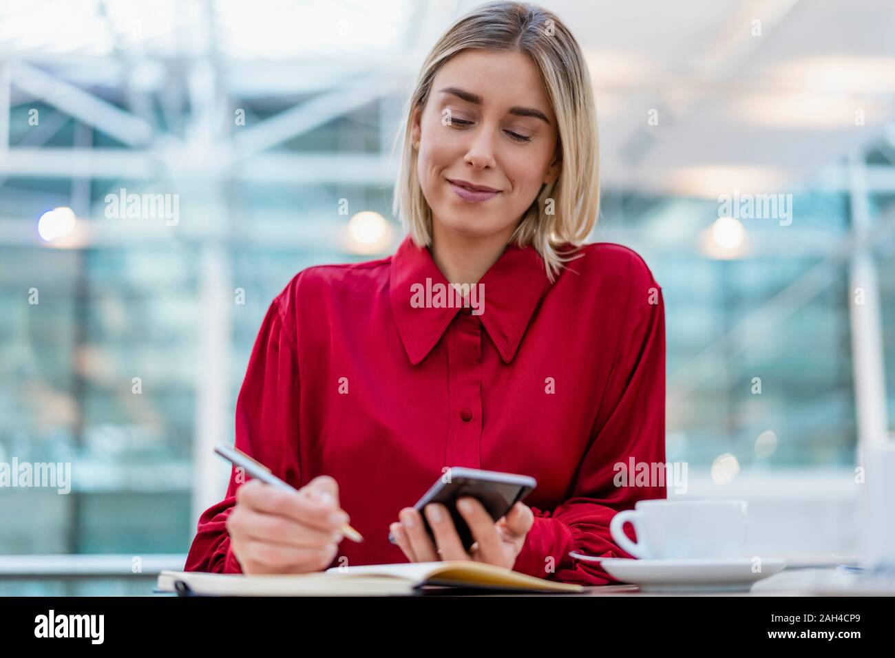 Joven Empresaria con teléfono celular tomando notas en la cafetería Foto de stock