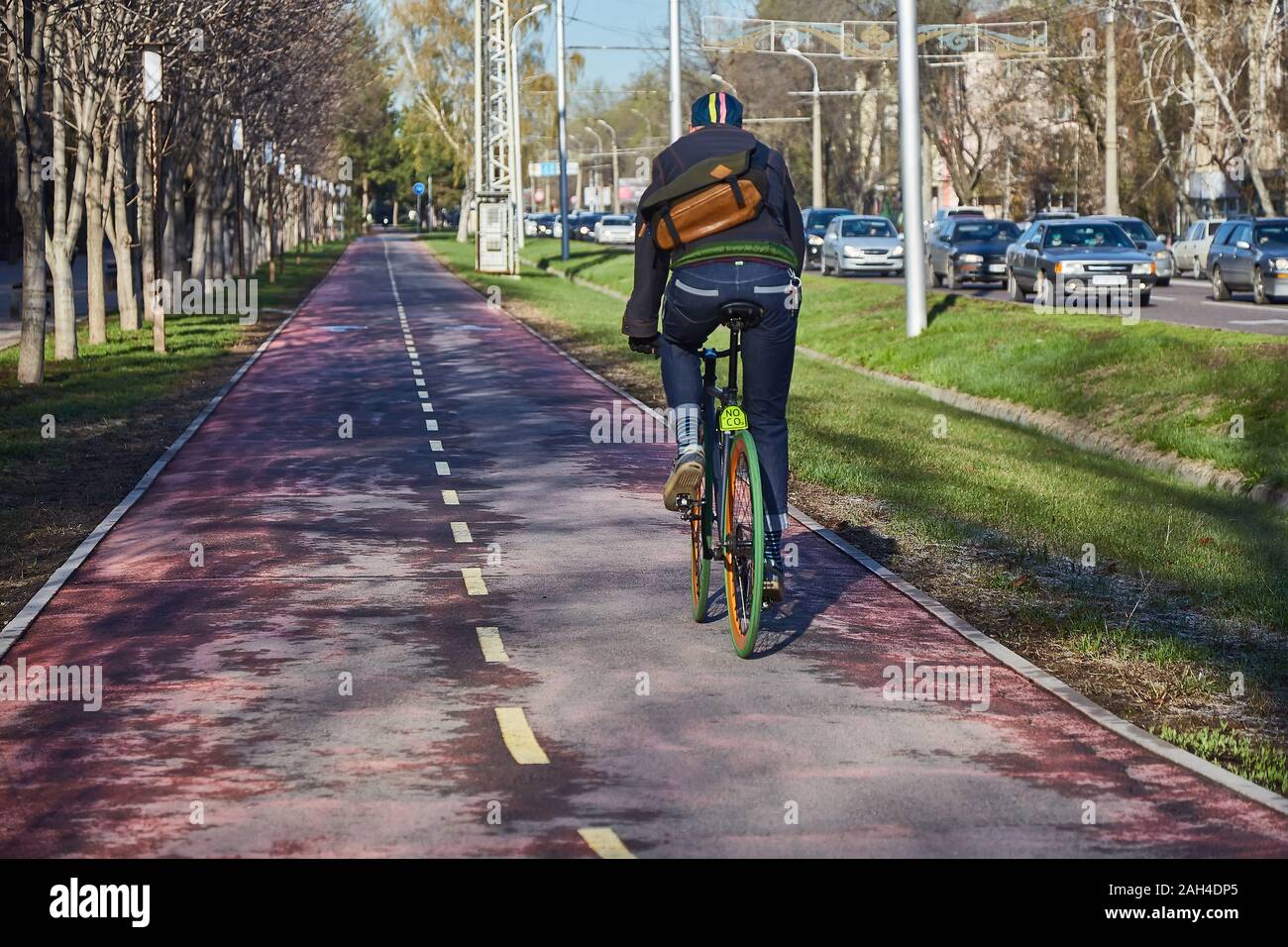 Un ciclista en la ciudad se está moviendo a lo largo de un camino para  bicicletas. Modo ecológico de transporte. Vista desde la parte de atrás.  Bicicleta con velocidad fija Fotografía de