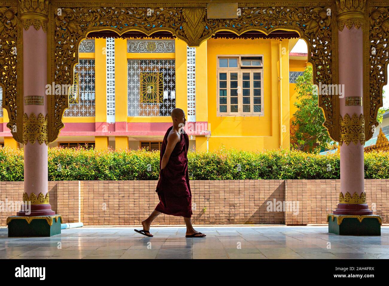 Monje caminando entre las columnas del templo dedicado a Buda reclinado en Yangon, Myanmar Foto de stock