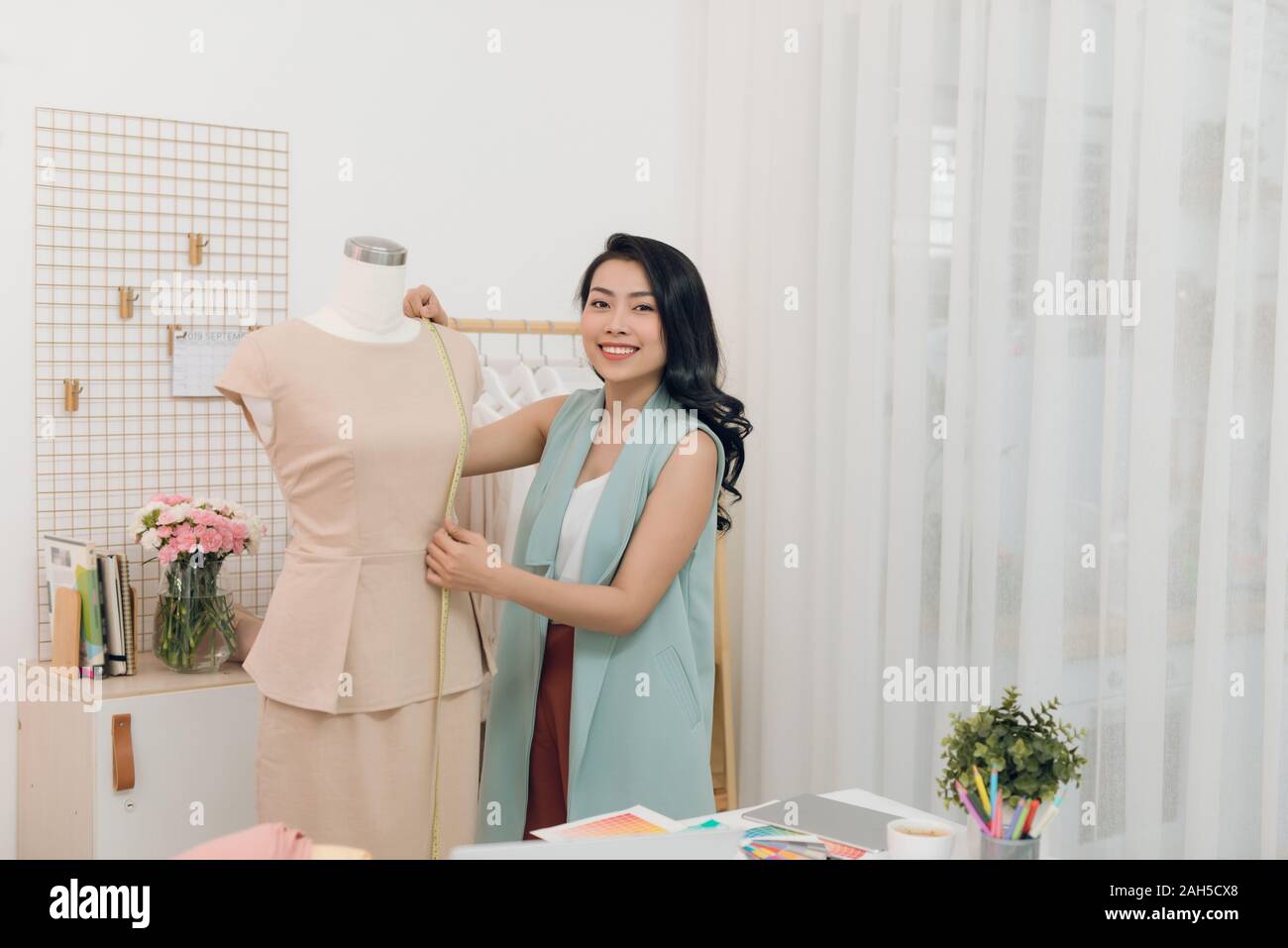 Una chica asiática está trabajando en el taller studio. Ella hace apenas sobre el vestido en el maniquí. Foto de stock