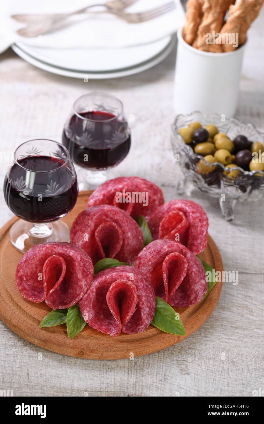 Comida ligera bocadillo de salami doblado en forma de flor con un vaso de vino de Jerez en un plato de madera. Foto de stock