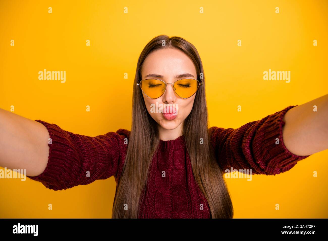 Cerrar Foto de chica encantadora en Gafas Anteojos enviar aire besos,  cerrando sus ojos vistiendo un suéter granate aislado sobre fondo amarillo  Fotografía de stock - Alamy