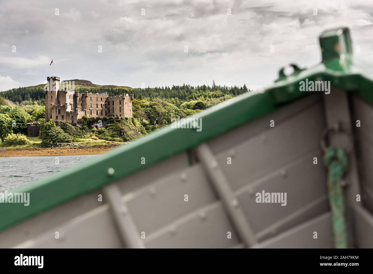 En primer plano la proa verde y gris de un barco de madera, en la distancia la costa de una isla escocesa con un antiguo castillo Foto de stock