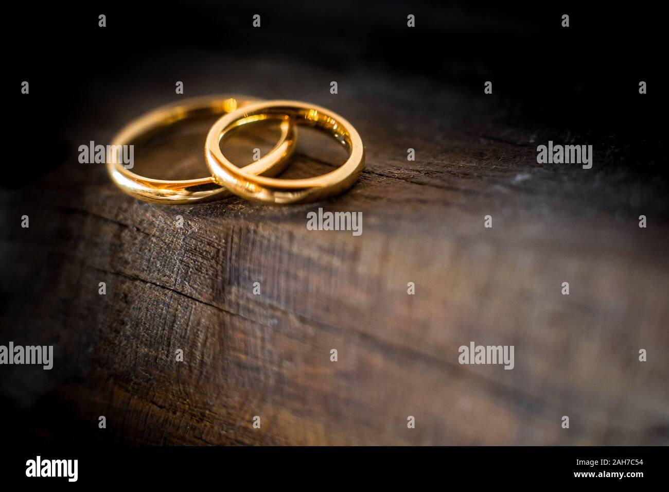 Primer plano de dos anillos de bodas de oro que yacen en el borde de una antigua y erosionada mesa de madera Foto de stock