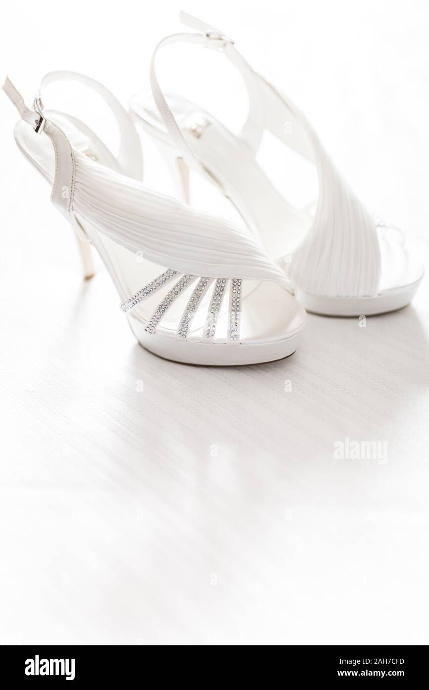 Primer plano de un par de zapatos blancos elegantes de tacón alto, tumbados en un suelo blanco Foto de stock