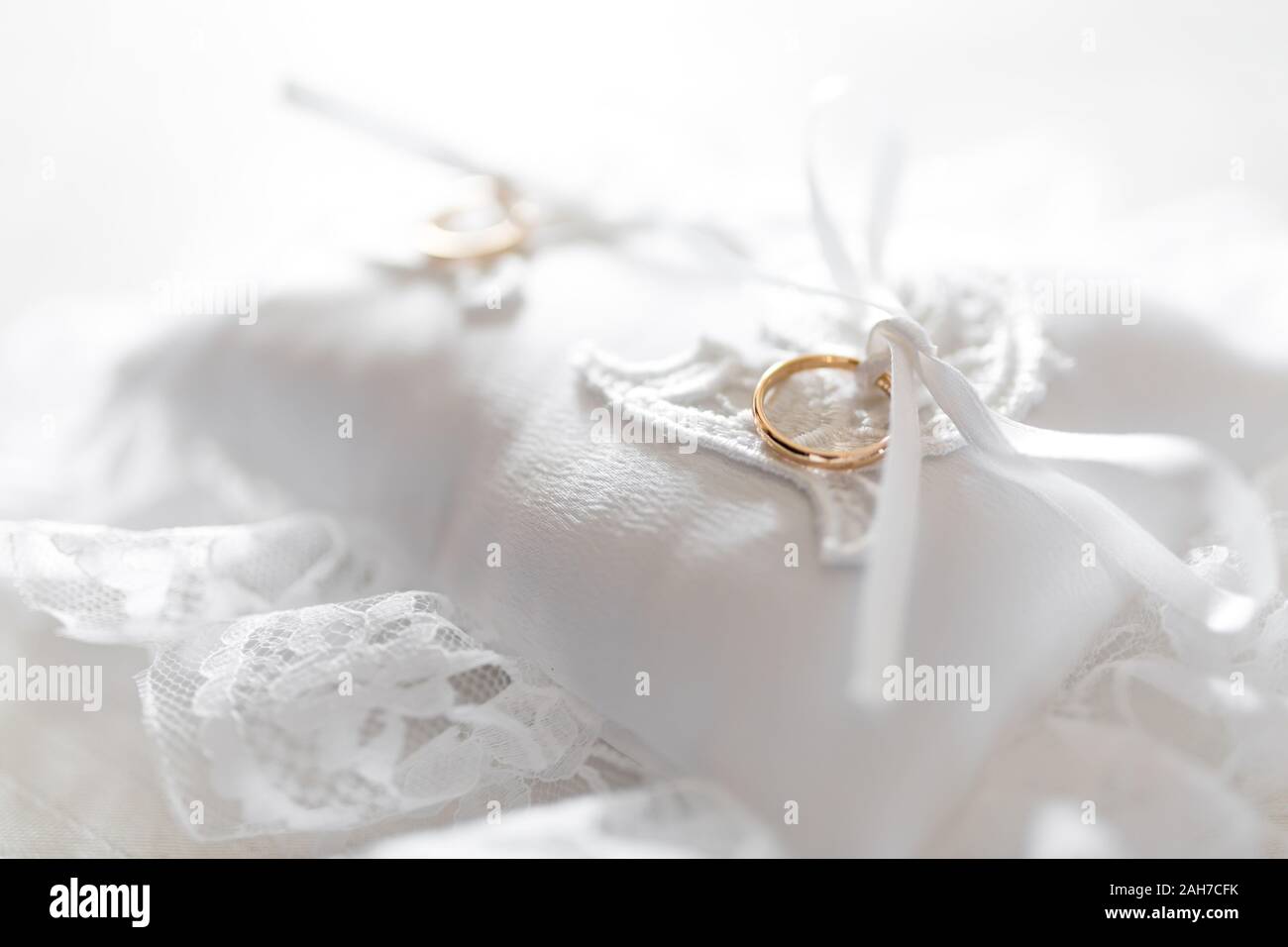 Primer plano de dos anillos de bodas de oro que yacen en un cojín blanco inundado de luz Foto de stock