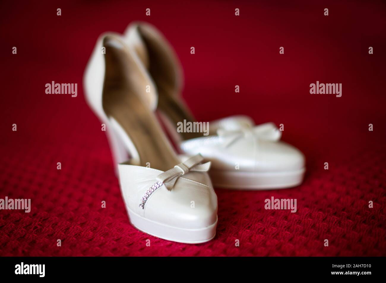 Primer plano de un par de blanco elegante high-heels boda zapatos sobre lino escarlata Foto de stock