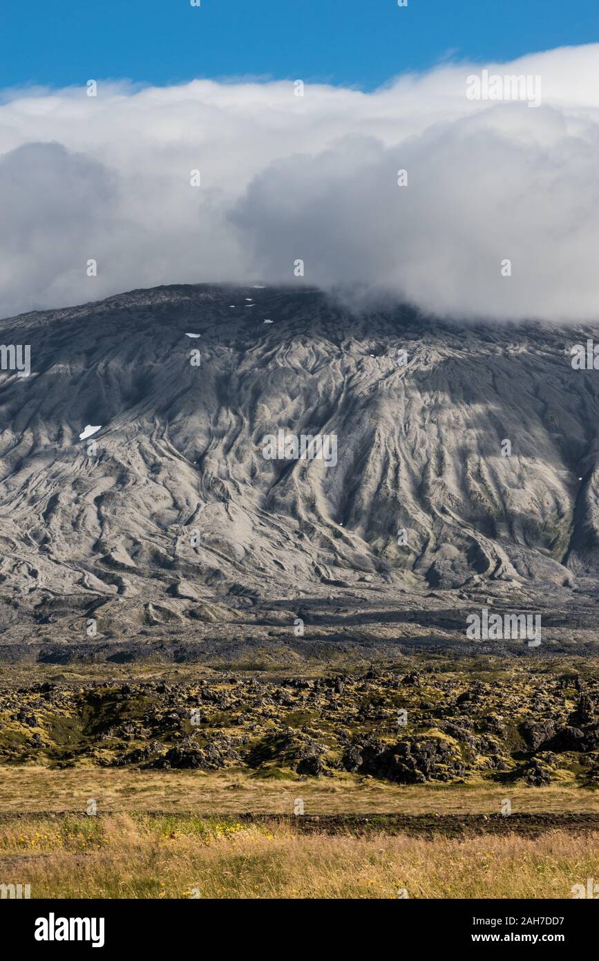 Icónico paisaje islandés, con una pared de montaña tallada por la erosión, bajo un cielo azul sólido de verano con una gruesa manta de nubes hinchadas Foto de stock