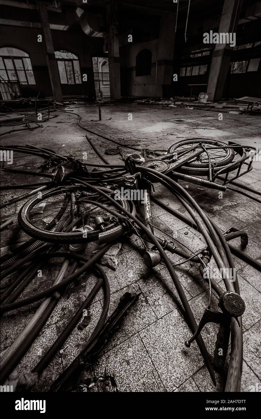 Vista en blanco y negro de gran angular de un suelo de fábrica abandonado, con una bicicleta desechada en primer plano Foto de stock