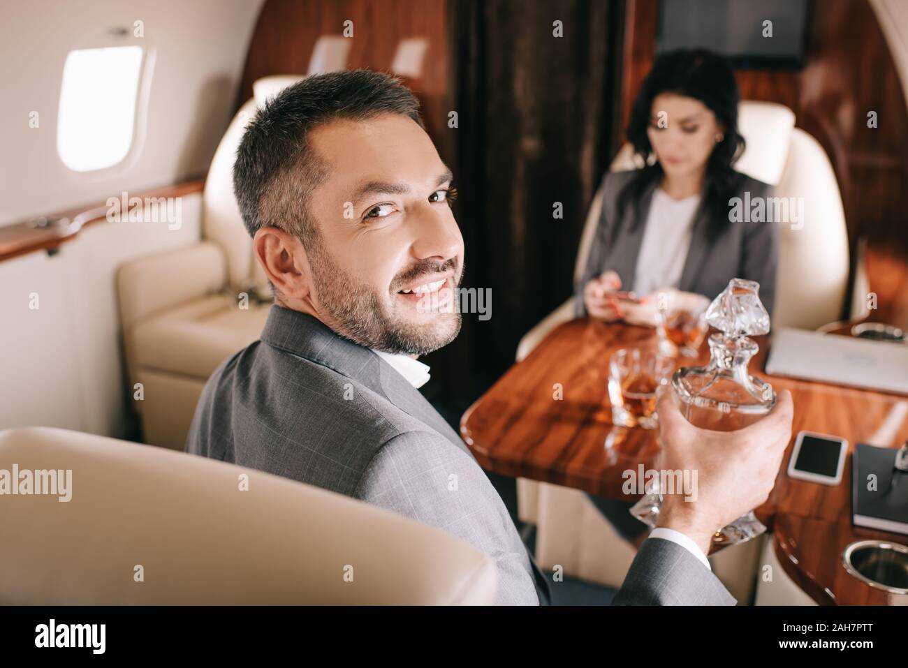 El enfoque selectivo de empresario feliz celebración frasco con alcohol beba cerca empresaria en jet privado Foto de stock