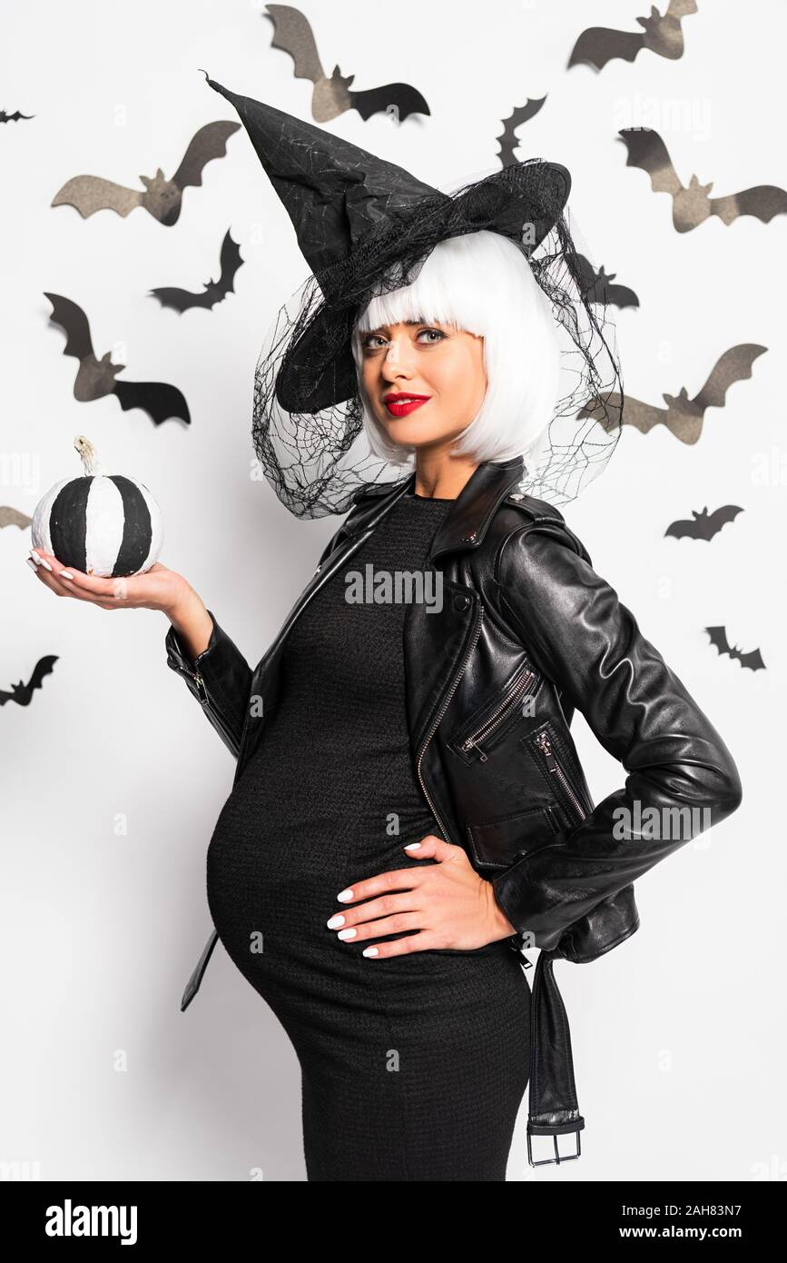 Mujer embarazada de bruja sombrero y peluca mantiene la calabaza en  Halloween Fotografía de stock - Alamy