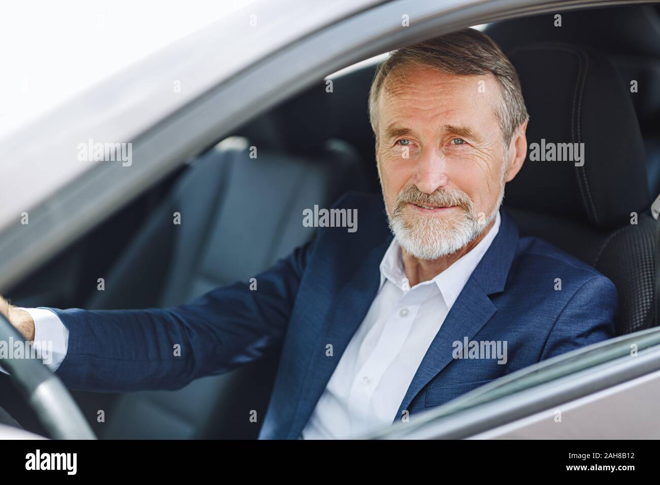 Senior conductor sentado dentro de un automóvil vistiendo ropas formales Foto de stock