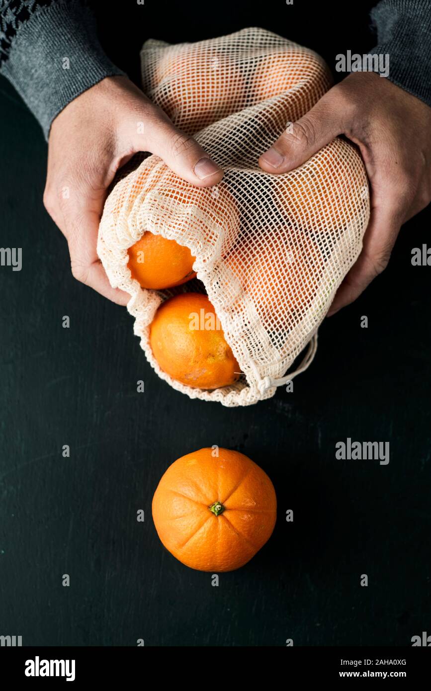Primer plano de un hombre sujetando una bolsa de malla reutilizables textiles, utilizado para comprar alimentos a granel, lleno de naranjas, como medida para reducir la contaminación plástica Foto de stock