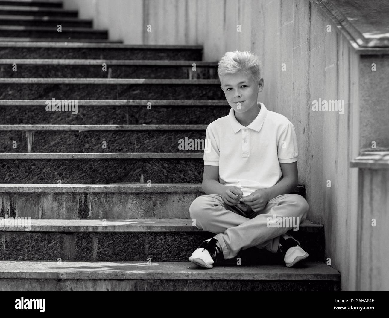 Monocromo (blanco y negro) retrato de lindo rubio guapo once viejo muchacho (adolescente) sentado en las escaleras al aire libre.Creciendo, chilhood, separando Foto de stock