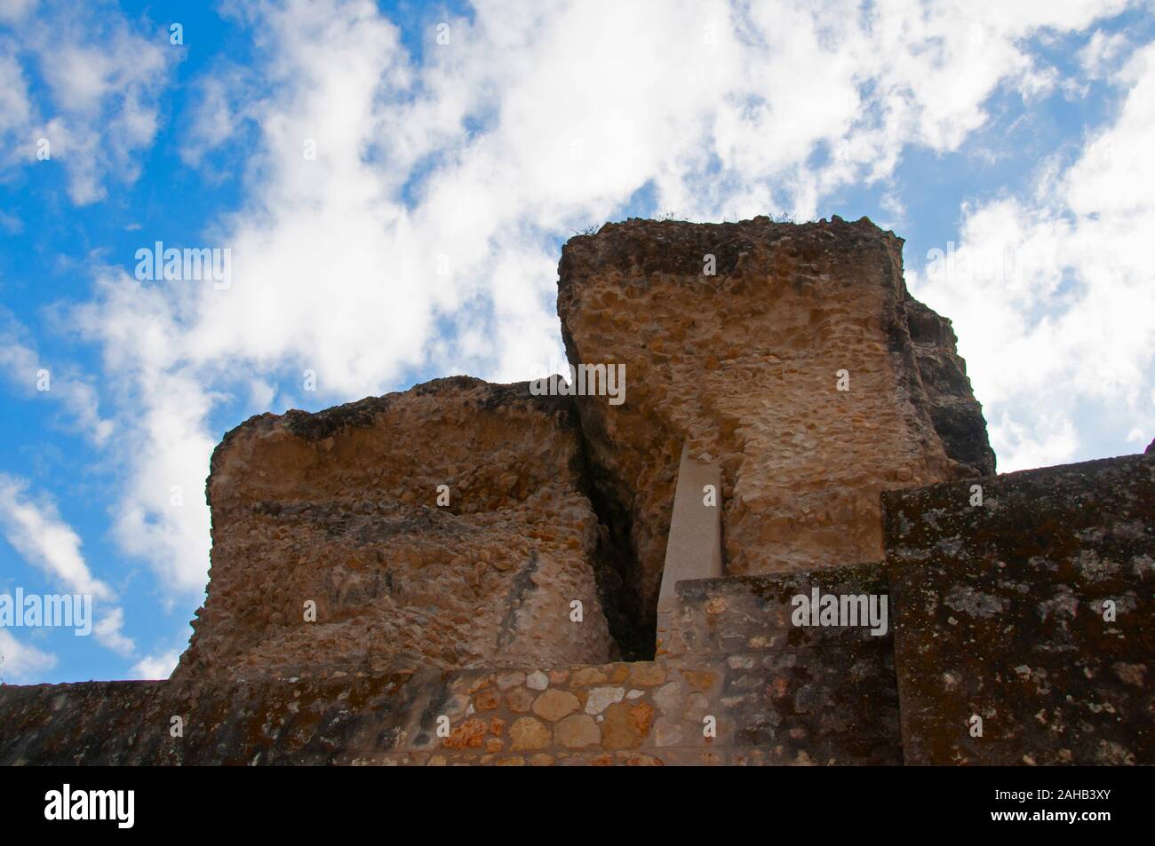 Dos grandes fragmentos de piedra del antiguo edificio romano y el muro de piedra. Cielo azul con nubes como fondo. Itálica, Sevilla, España Foto de stock