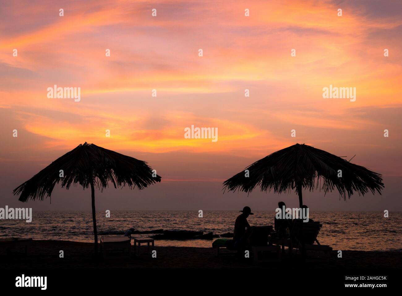 Silueta de sombrillas y gente sentada y disfrutar de la puesta de sol  dorado en Goa, India. Chill out al atardecer, vacaciones de verano relájese  concepto Fotografía de stock - Alamy
