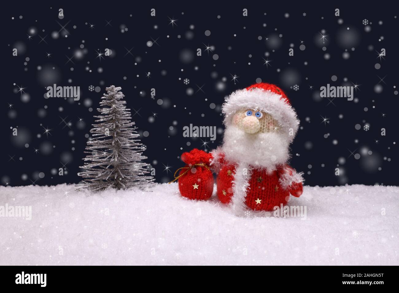 El juguete de lana de punto Santa Claus está de pie al lado Un árbol de  Navidad de plata de juguete sobre nieve blanca artificial contra fondo azul  marino Fotografía de stock -