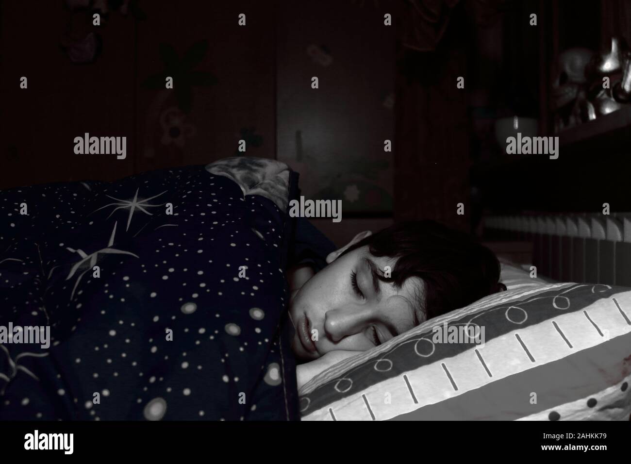 Un muchacho caucásico duerme en la cama de su dormitorio cubierto por una colcha con un motivo espacial Foto de stock