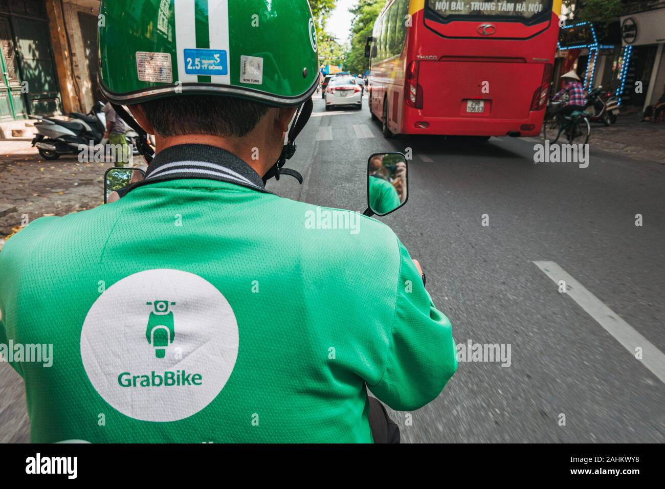 La vista desde la parte trasera de una bicicleta de agarre como el jinete lleva tráfico en Hanoi, Vietnam, vistiendo un casco con la marca de la empresa y la camisa Foto de stock