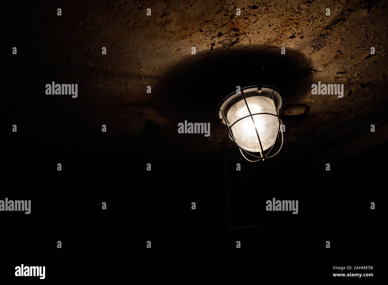 Sucio imagen con la luz de la bombilla y una red metálica sobre un techo desgastado en una antigua celda de prisión. Foto de stock