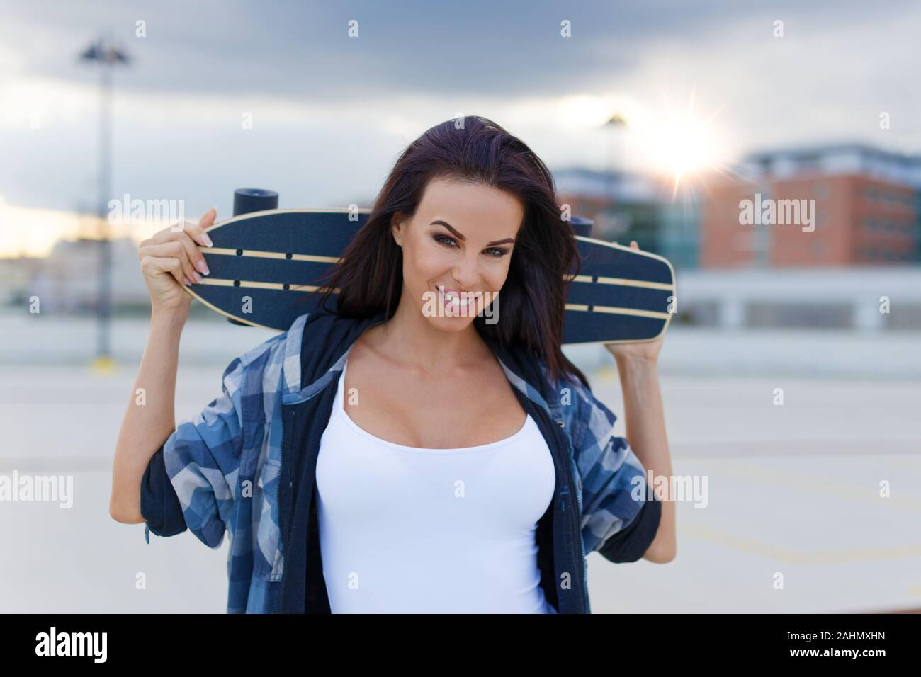 Los jóvenes urbanos de moda mujer sosteniendo longboard detrás de su cabeza Foto de stock