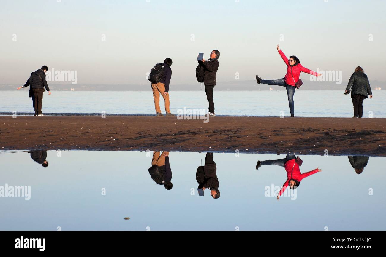 Playa de Portobello, Edimburgo, Escocia, Reino Unido. El 31 de diciembre de 2019. Tras una helada noche una temperatura de -1°C con pleno sol no moleste estos visitantes en este último día de 2019, los visitantes se reflejan en el agua del mar dejada por la marea saliente. Foto de stock
