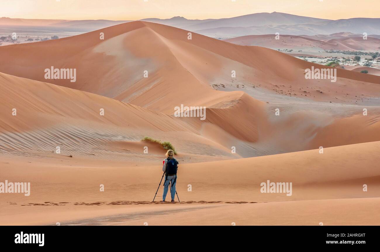 Sossusvlei, Namibia - Agosto 26, 2016. Una mujer fotógrafo toma fotos de grandes dunas de arena en el desierto de Namib al amanecer. Foto de stock