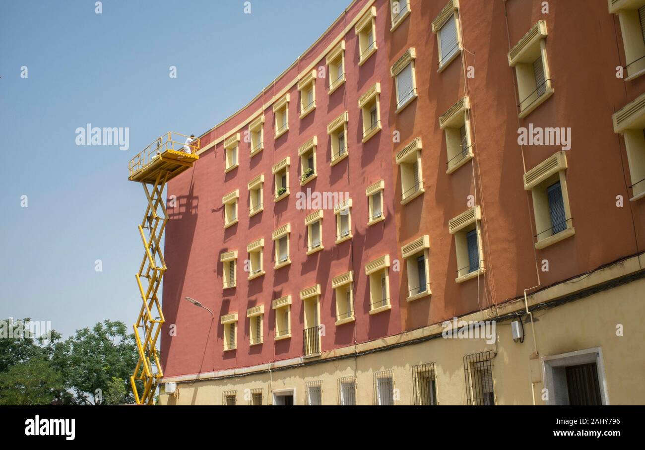 Pintor trabajando sobre la plataforma elevadora de tijera. Fondo urbano sobre un cielo azul. Badajoz, España Foto de stock