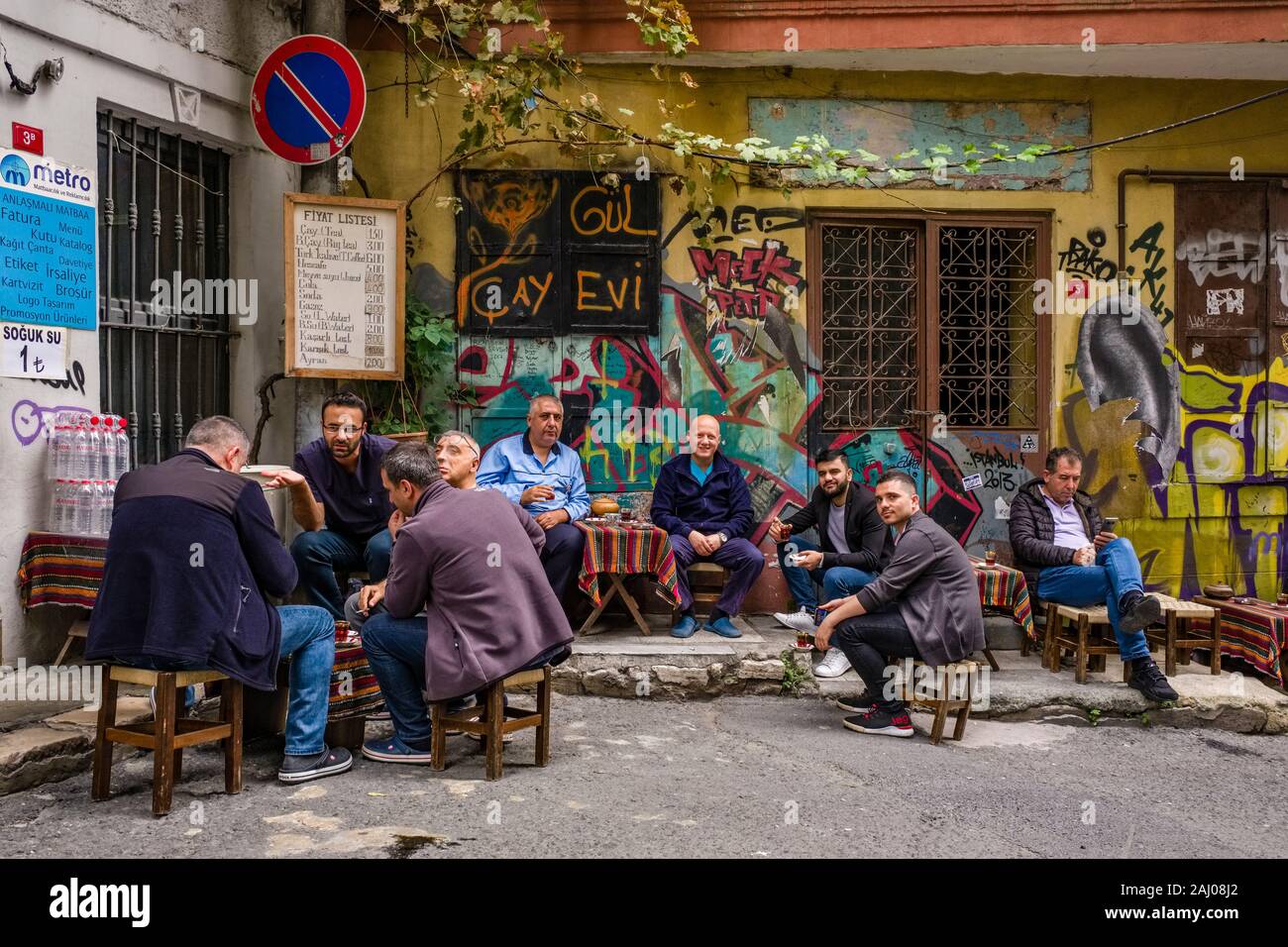 Muchos hombres están sentados fuera de una tienda de té, beber té, la fachada de una casa con graffity rociado sobre detrás en el suburbio Karaköy Foto de stock