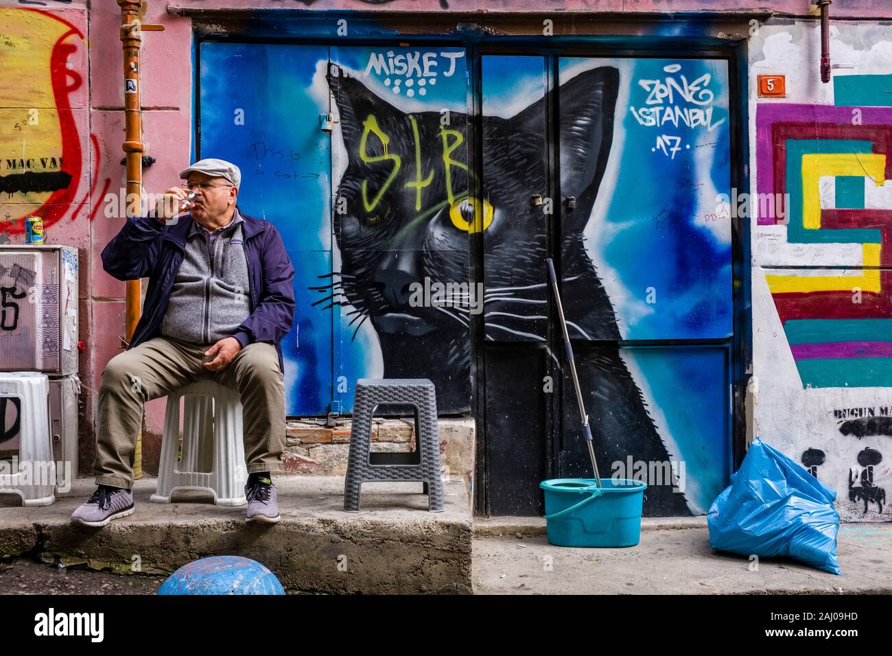 Fachada de una casa con graffity de rociado sobre el retrato de un gato, un hombre mayor de edad beber té delante de él en el suburbio Karaköy Foto de stock