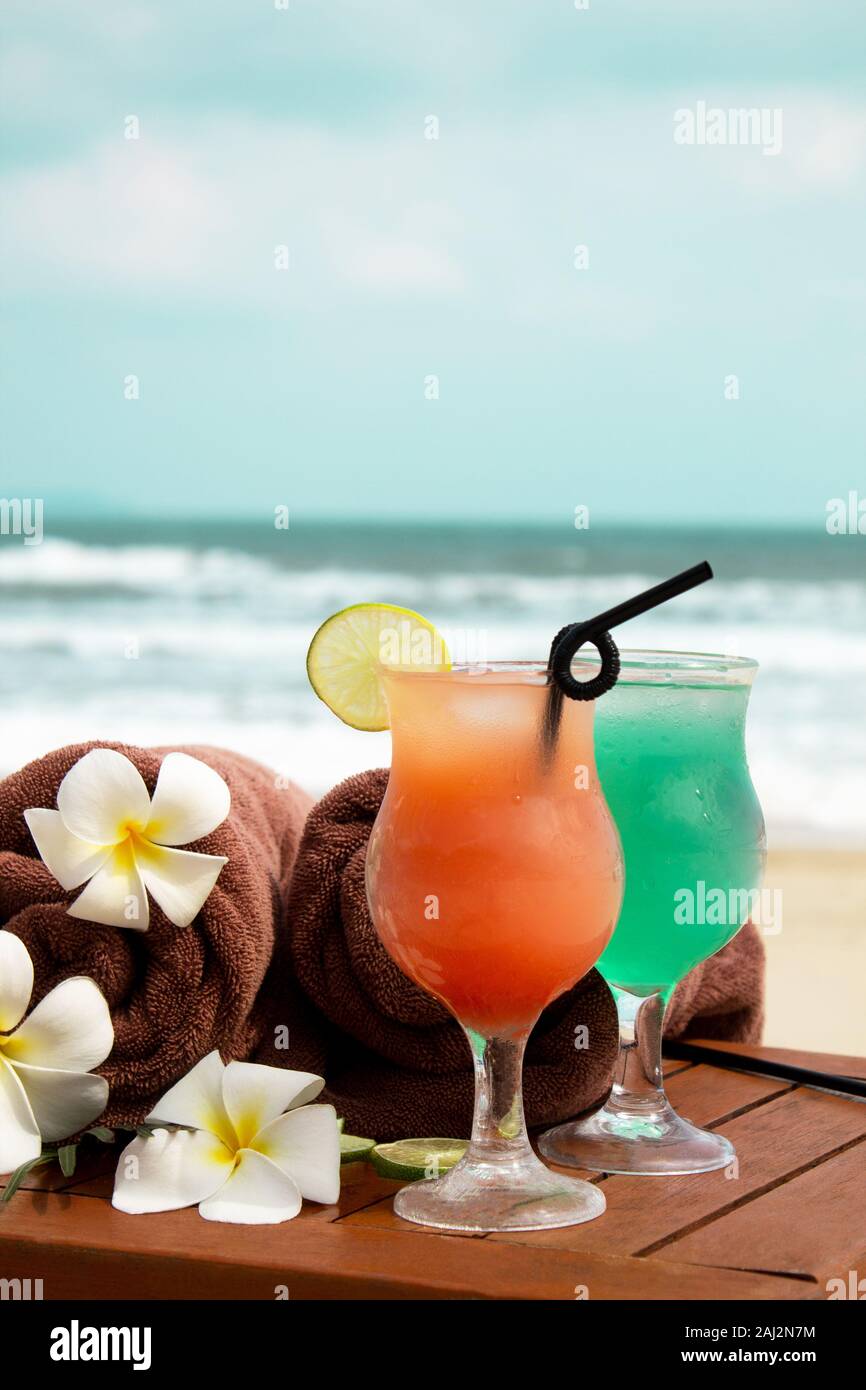 Hielo Tropical verano y cócteles, toallas femeninas y un paja en una playa de arena en un fondo de mar azul. Copie el espacio Fotografía de stock -