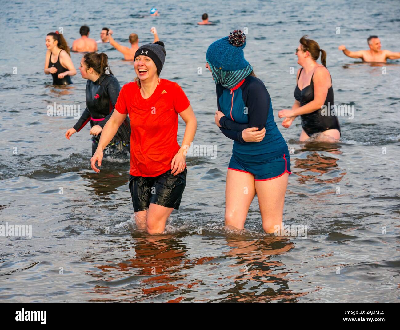 La gente en el mar para Año Nuevo 2020 Loony Dook o Dip con dos jóvenes mujeres riendo, North Berwick, East Lothian, Escocia, Reino Unido Foto de stock