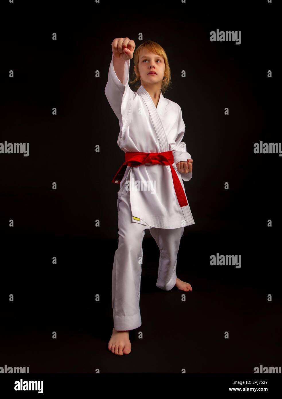 Niña en un kimono de deportes y un cinturón rojo realiza ejercicios en kata  sobre un fondo oscuro Fotografía de stock - Alamy