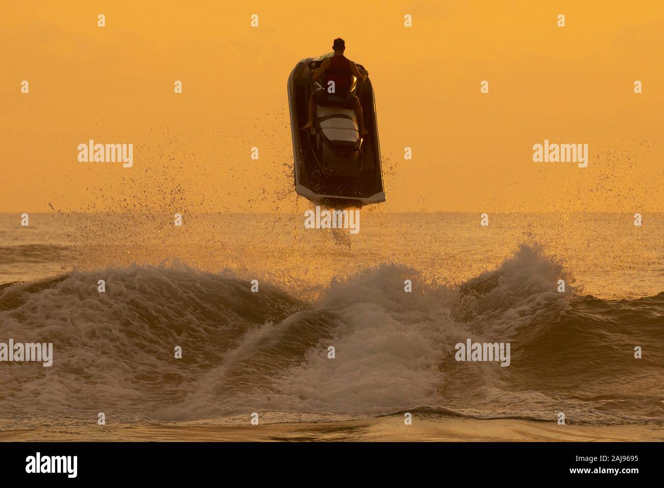 Silueta de hombre montado en una moto de agua y saltando sobre una ola de sunrise Foto de stock